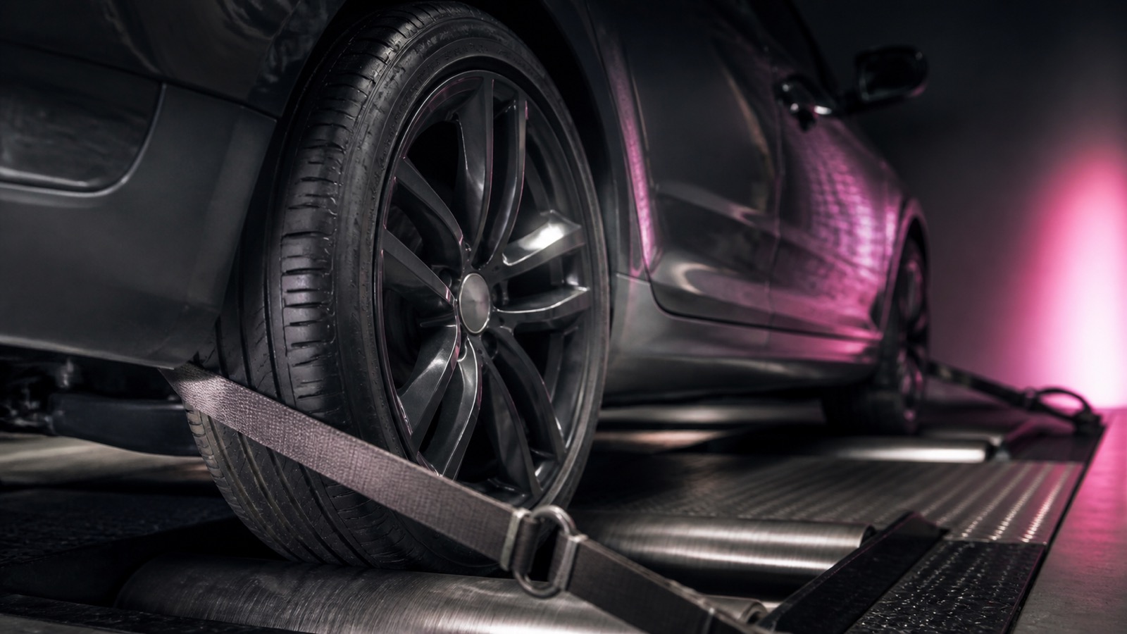 Car wheel strapped down on rolling road dynamometer rollers